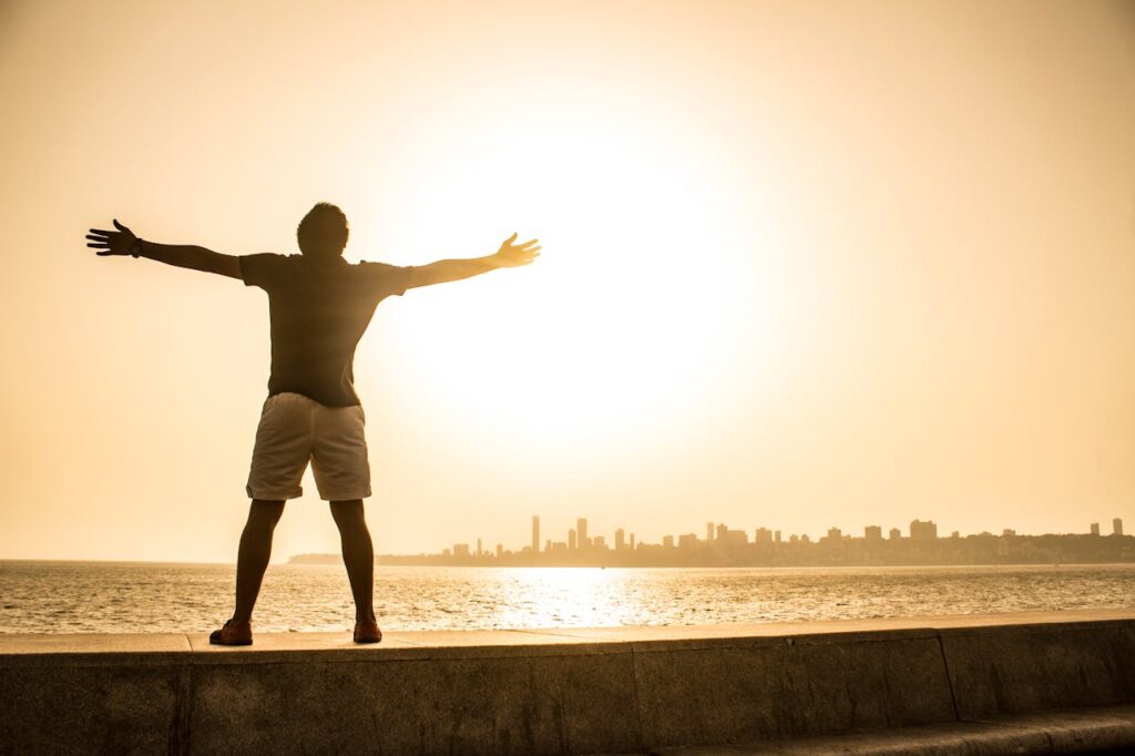 Man stands with arms outstretched facing the sunset over the ocean, capturing a moment of freedom and tranquility.