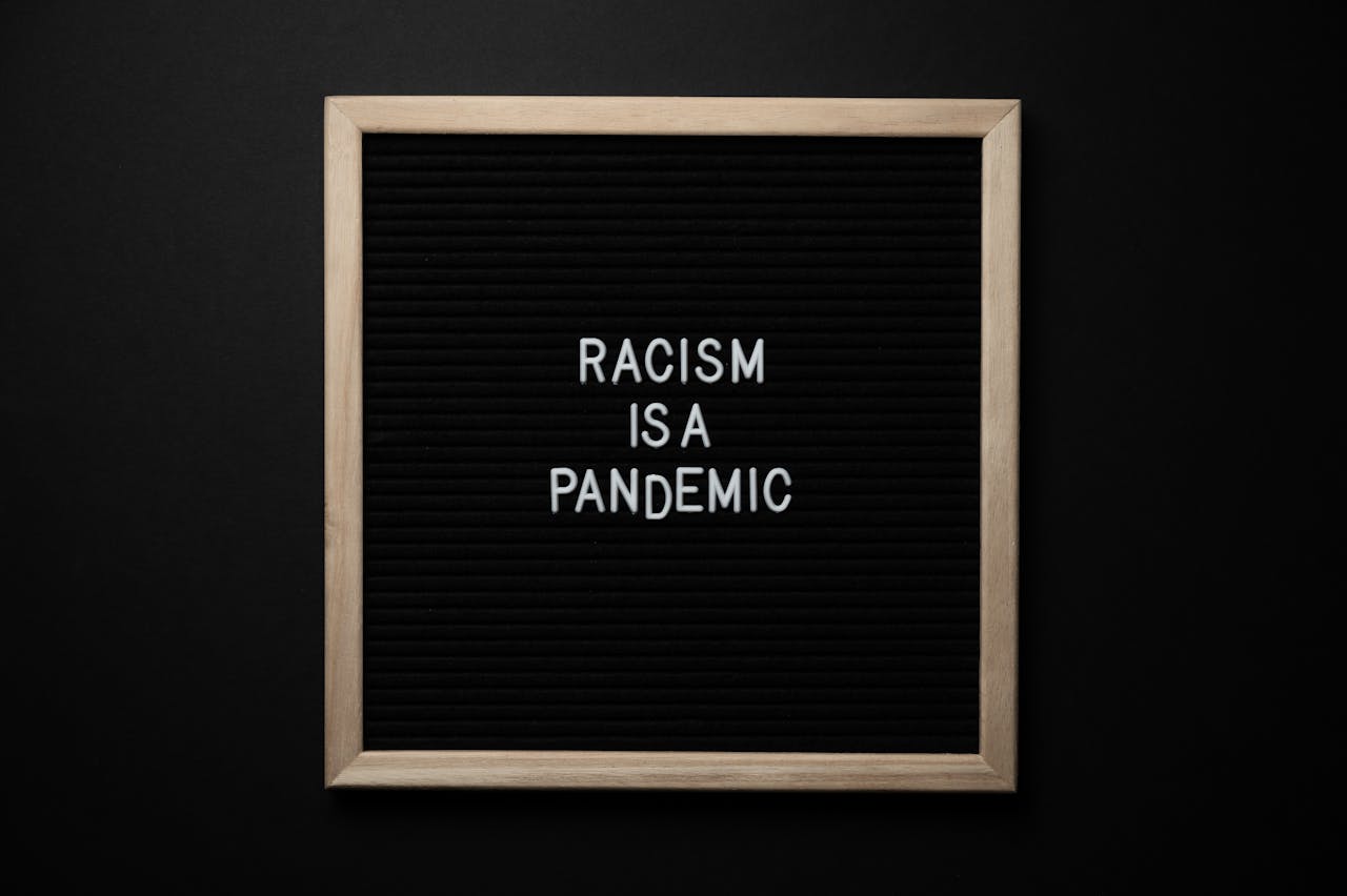 Overhead view of slogan Racism Is Pandemic on black square signboard in light of lamps on black background